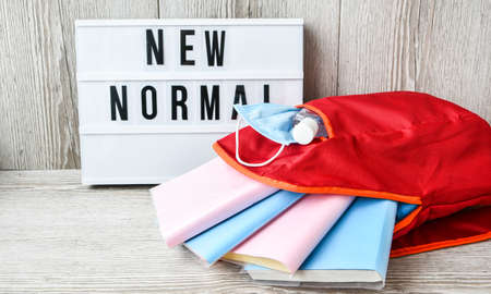 Lightbox with text NEW NORMAL protective face mask and sanitizer. Back to school. Books falling from...
