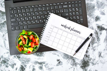 Exercise plan for a week. Bowl with vegetable salad in the workplace near the computer. Lunch in the...