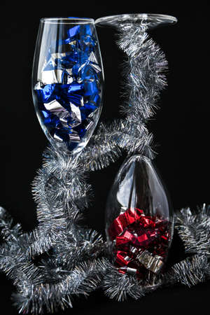 Two champagne glasses with holiday confetti on black background, new year and christmas decorations, copy space for textの写真素材