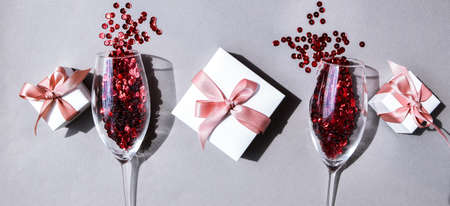 banner two champagne glasses with confetti and gift boxes isolated on an empty pink festive background, copy space, valentines day, Christmas and New Year or holiday festive cardの写真素材
