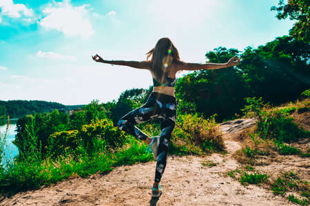Woman Doing Yoga On Mountain Against Sky and Sun. Hard light. Silhouette of girl doing outdoor sport stretch. practicing yoga. meditating on mountainの写真素材