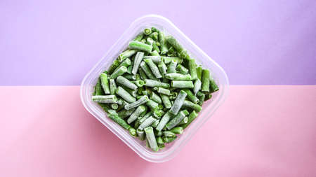 Frozen green beans in a plastic container for long-term storage. Deep freezing of vegetables. Frozen food vegetables on color background. Copy space for text. Stocking up vegetables for winter storageの写真素材
