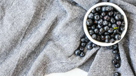 Small White Bowl of Organic Blueberries on Wooden Table with kitchen towel. Copy space. Summer fruit berries. Fresh forest berryの写真素材
