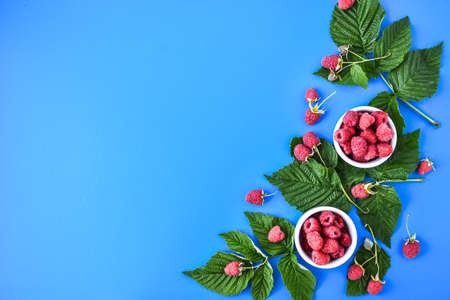 Red fresh raspberries with green leaves on blue background. Top view, flat lay, copy space for text. Summertime fresh berries.の写真素材