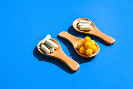 Pills and capsules on wooden spoons on blue background. Hard light and shadows. Copy space. Vitamins...