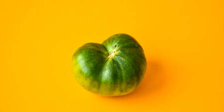 Trendy ugly organic vegetables. Green tomato on yellow background. Cooking ugly food concept. Top view. Copy space for text.の写真素材