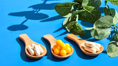 Pills on wooden spoon on blue background. Hard light and shadows. Creative minimalism concept. Vitamins and prebiotics, probiotics. Autumn vitamin dose. Eucalyptusの写真素材