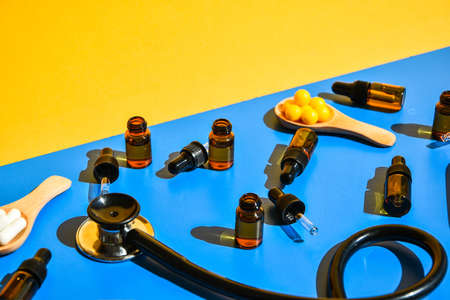Pills on wooden spoon and dropper pipette on blue and yellow background. Hard light and shadows. Modern isometric creative minimalism concept. Vitamins and prebiotics, probiotics. Autumn vitamin dose.の写真素材