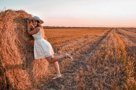 Portrait of young happy smiling woman on the haystack in sunset, countryside. The concept of freedom of joy of discovery and fresh air in nature. Cottagecore. relaxing on summer field with hay stacks. Fresh air contryside. pastoral lifeの写真素材