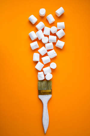 White marshmallows on yellow background with painting brush. Creative concept of unheathy junk food. Food sweets background.の写真素材