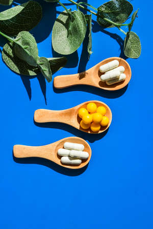 Pills on wooden spoon on blue background. Hard light and shadows. Creative minimalism concept....