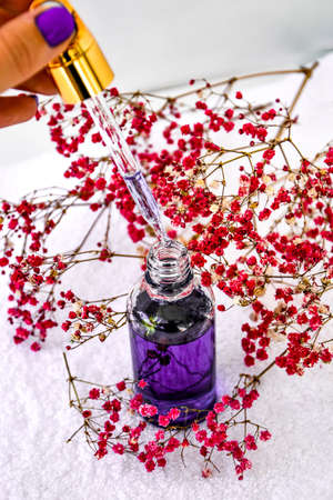 Woman dripping rose essential oil Glass dropper of cosmetic oil and dried flowers and herbs on white background. Natural organic herbal skin care oil, spa towel, small pink flowers. Facial liquid serum with collagen and peptides. Skin care essenceの写真素材