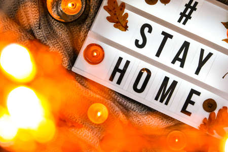 Hashtag Stay home. Text in white light box, with a background of sweater, candles, dried leaves autumn decoration. Coronavirus devices. Social distancing. Protection against pandemics. Stay safe. Cozy homeの写真素材