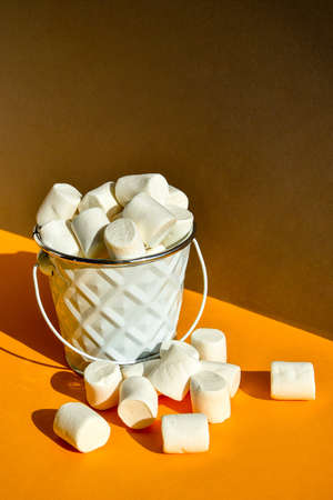 White marshmallows in metal bucket on a yellow and gray modern background, an ingredient for making a Christmas drink and decorating cakes, vertical orientation. creative food background. Junk unhealthy food.の写真素材
