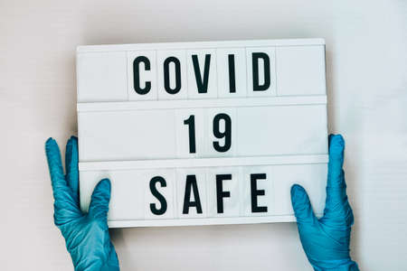 Doctor in protective gloves holding Lightbox with text COVID 19 SAFE. Back to school. Social distancing. School quarantine concept. Copy space. Coronavirus second waveの写真素材