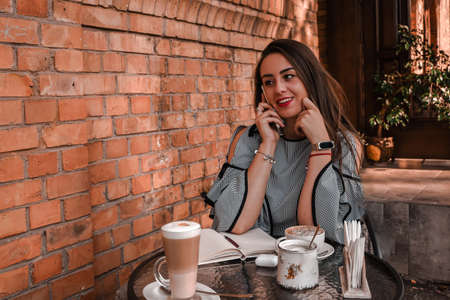 A young brunette woman sitting in a coffee shop, drinking coffee, and using smartphones.の写真素材