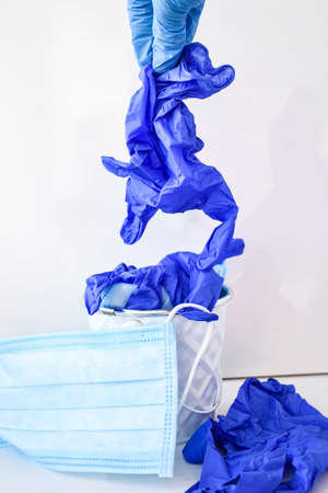 Hand throwing away used infectious masks and medical glove in the trash bin. Coronavirus trash....