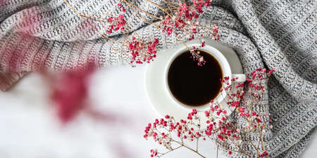Cup of black coffee on white background with sweater and bright pink flowers. Flat lay. Copy space. Fashion concept. Cozy lifestyle. Still lifeの写真素材