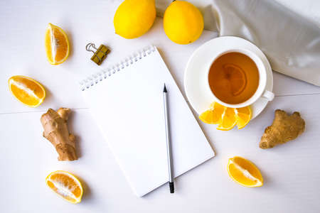 Trendy flat lay Ginger hot immunity boosting Vitamin natural drink With citrus lemon notebook and pencil on white background. Copy space. Healthy concept. top view.の写真素材