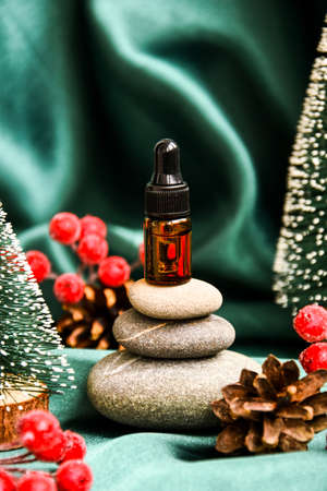 Small bottle of serum on stack of basalt stones with christmas decorations on green satin fabric background. Trendy color. Beauty pipette dropper on pyramid of pebbles. natural medicine, nose drops, eye dropsの写真素材