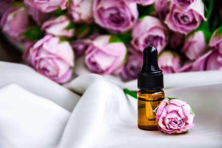Rose oil. Spa and aromatherapy rose flowers essential oil bottle with pipette on satin champagne color fabric. Bottles of rose essential oil and fresh flowers. Copy spaceの写真素材