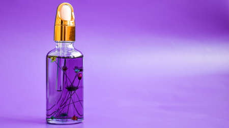 Dropper glass Bottle with flowers inside Mock-Up. Cosmetic pipette on purple background. Cuticle oil, Anti aging serum in glass bottle with dropper Skin care essence for beautiful healthy skin copy spaceの写真素材