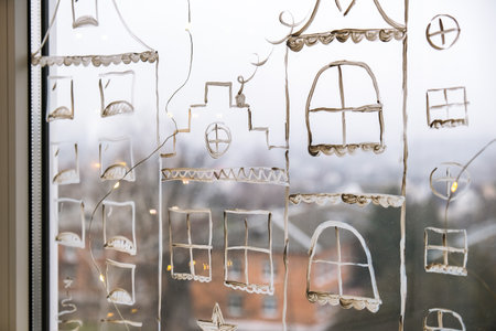 christmas holidays decoration painted on window glass. New Years scenery. city buildings garlands lights. hygge, decoration and christmas concept. festive garland string at homeの写真素材