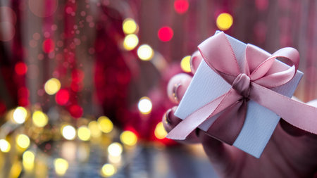 Christmas gift in the hand of a woman on garland bokeh light. Selective focus. Valentines present....