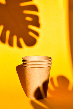 Paper coffee containers on yellow background with hard shadows of palm leaf. Paper cups. Copy space. No plastic. Plastic free. Zero wasteの写真素材