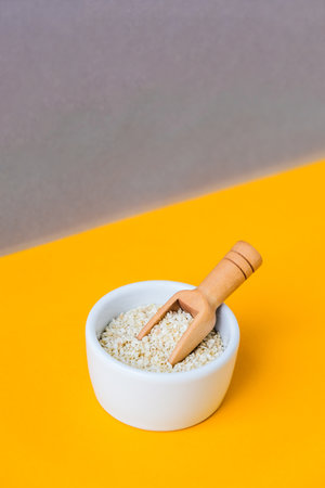 Wooden spoon with sesame seeds lies in a white mortar on a yellow background. Healthy eating. Keto diet. Trendy vegan food. Minimalistic concept in isometric style in trendy colorsの写真素材