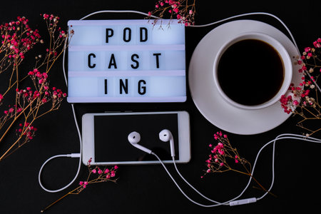 Podcasting lettering. Headphones mobile phone. Dry pink flowers decoration. Workplace. Black coffee. Podcaster, podcast Audiobooksの写真素材