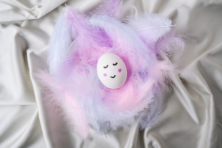 Diy for kids. Do it yourself. Funny painted smiley egg face in bird feather. Easter decorations. Copy space for text. Pastel colors. Easter greeting card.の写真素材