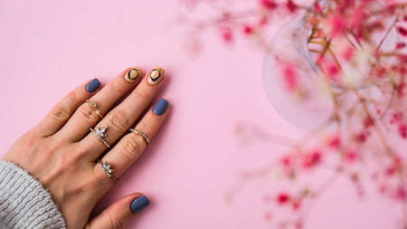Hand in sweater and pink flowers with modern manicure nails. Female hand. Glamorous beautiful manicure. Manicure salon concept. Nail polish close up.の写真素材