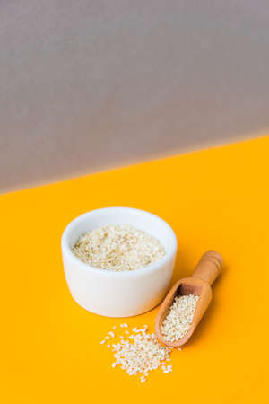 Wooden spoon with sesame seeds lies in a white mortar on a yellow background. Healthy eating. Keto diet. Trendy vegan food. Minimalistic concept in isometric style in trendy colorsの写真素材