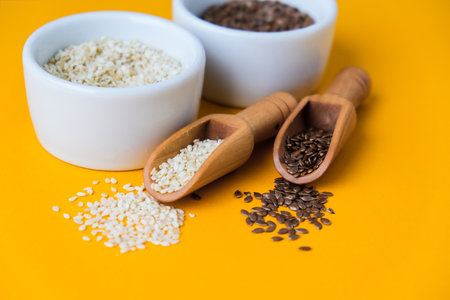 Wooden spoons with sesame and flax seeds lies in a white mortar on a yellow background. Healthy eating. Keto diet. Trendy vegan food.の写真素材