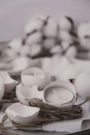 Trendy Easter decorations. Cracked organic eggs on plate. Candle in White shell of the eggs. Bird...