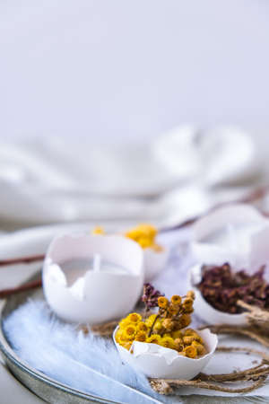 Easter DIY. Do it yourself. Trendy Easter decorations. Cracked organic eggs with dry grass and dry flowers on plate. Candle in White shell of the eggs. Bird feather. Copy space. Greeting card. Pastel colors.の写真素材