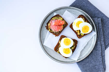 Three sandwiches on plate. Guacamole toast with eggs and salmon. Vegetarian healthy food. Healthy eating. Diet. Sesame seeds.の写真素材