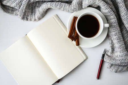 Cup of coffee with notebook cinnamon sticks and anise star on white background. Sweater around....