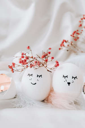Easter DIY do it yourself. Minimal easter concept. Easter eggs with painted smiley faces and bird feather on pastel background. Married. Valentines day Wedding couple eggs. Easter holiday concept with funny faces handmade eggsの写真素材