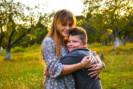 Young mother hugging and kissing her son in summer or autumn park. Family love first. Happy family...