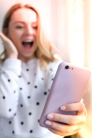 Blonde young girl taking selfie. Video call. Online education. Work from home. Woman holding smartphone. Phone call. Recording new vlog for her channel. Blogger Conference surprisedの写真素材