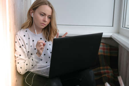 Young woman sitting on balcony next to laptop. Online education. Stay home concept. Work from home. Earphonesの写真素材