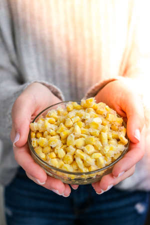 Female hands holding bowl with Frozen yellow corn. Vegetable preservation. Harvest. Veganism, vegetarian healthy eating. Fitness dietの写真素材