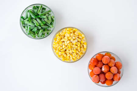 Three Bowls of frozen vegetables food of yellow corn, green beans, red tomatoes. Colors of traffic...