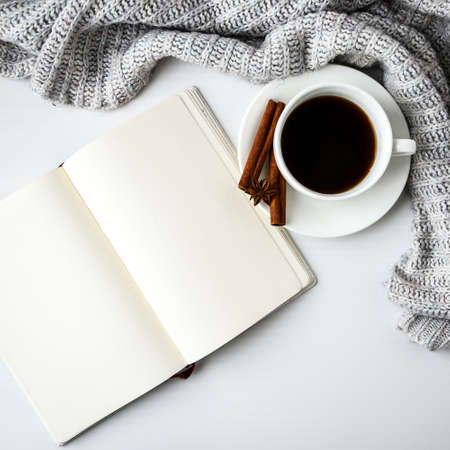 Cup of coffee with notebook cinnamon sticks and anise star on white background. Sweater around. Winter morning routine. Coffee break. Copy space. Top view. Breakfast. Flat layの写真素材