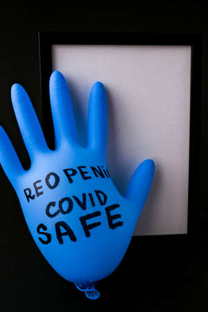 Blown up blue latex surgical glove on black background. Reopening safe. Open again text written on medical glove. New normal.の写真素材
