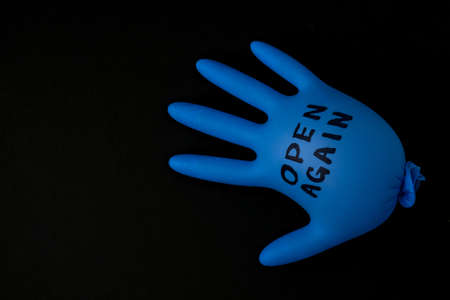 Blown up blue latex surgical glove on black background.  Open again text written on medical glove. New normal.の写真素材