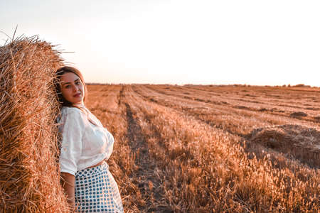 Portrait of young sexy woman on the haystack in morning sunlight, countryside. Beautiful woman in a...
