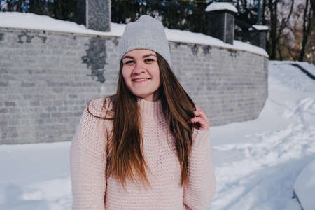 Beautiful young woman in knitted sweater in winter park. Cold weather outdoors. Snow Happy smiling portrait of girl. Winter fashionの写真素材